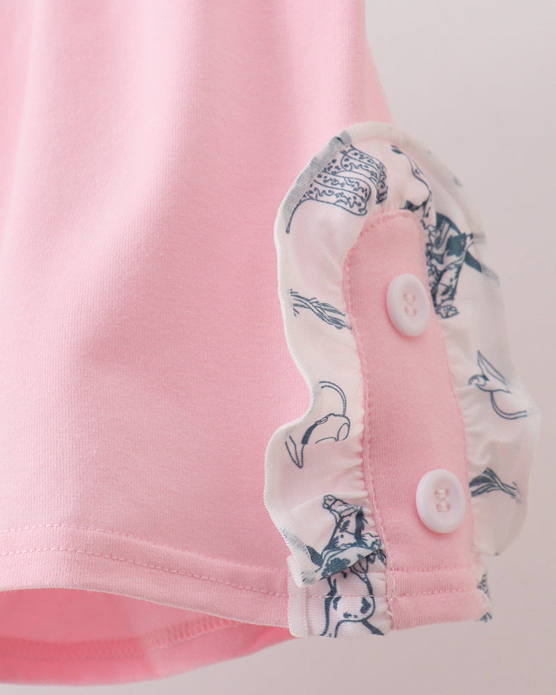 Close-up of a pink garment with a floral trim and buttons on a light background