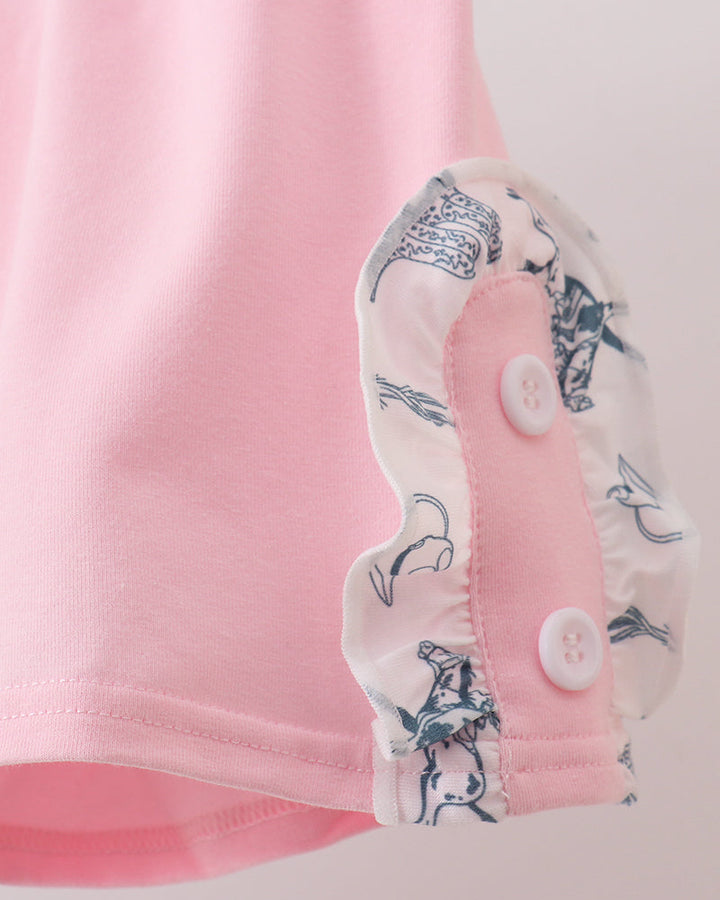 Close-up of a pink garment with a floral trim and buttons on a light background