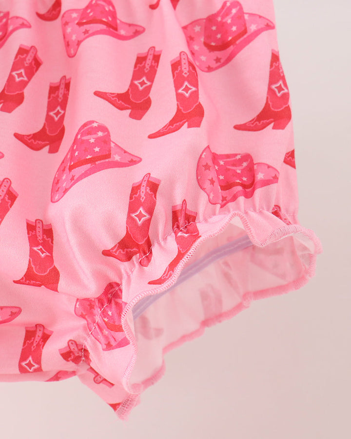 Pink fabric garment detail with an allover red cowboy boot and hat print, shown against a pale pink background.
