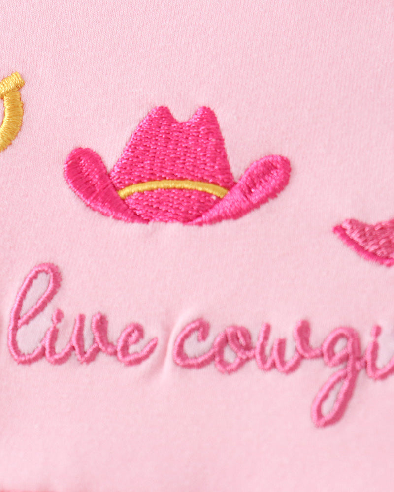 Close-up of a pink embroidered textile with a pink cowboy hat outlined in yellow and the partial phrase &