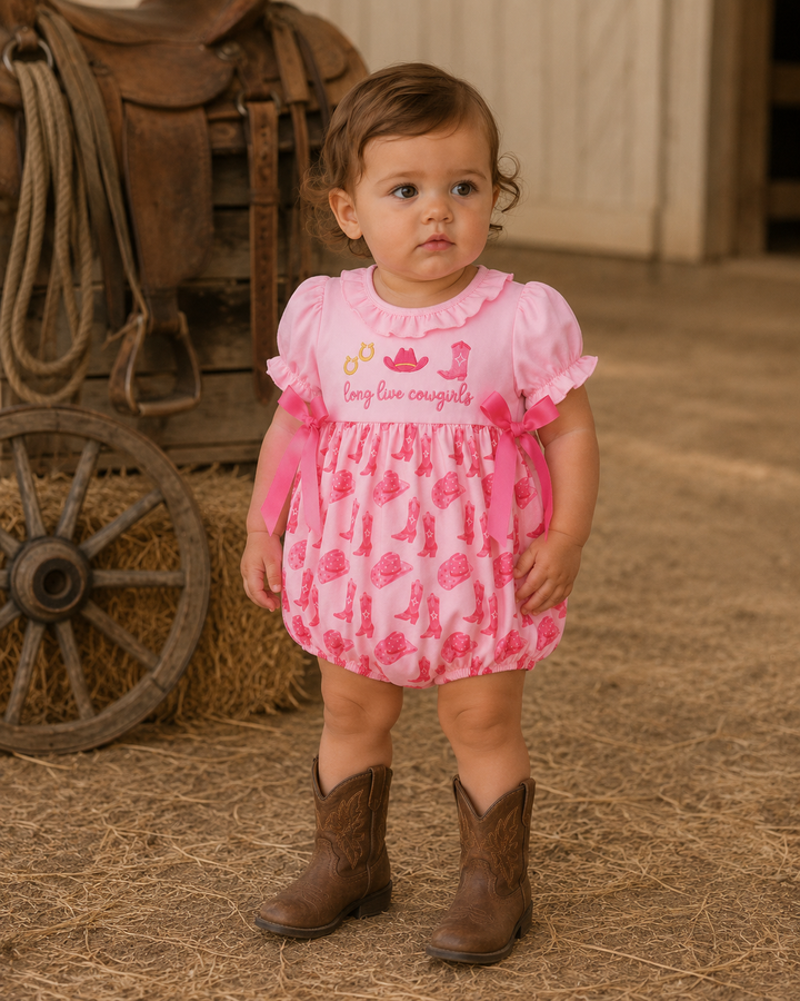 A toddler girl wearing a pink short-sleeve romper with a cowboy boot print and &