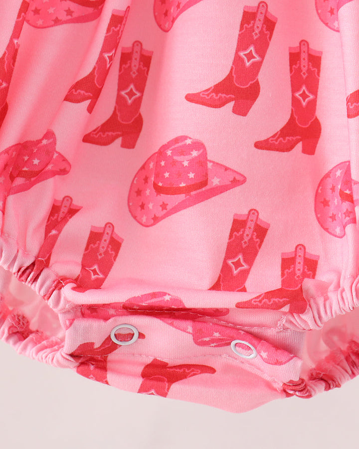 Pink fabric garment with an allover cowboy boot and cowboy hat print, shown close up with elasticized ruffled trim and snap closures at the bottom.