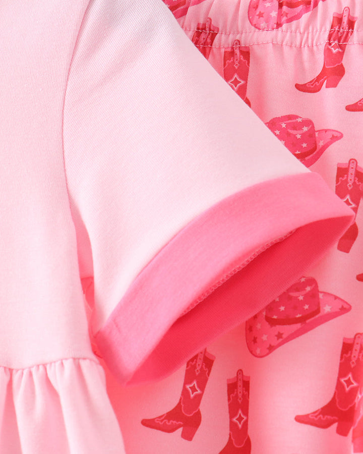 Close-up of a pink garment with a solid light pink sleeve featuring a darker pink cuff, layered over a pink patterned fabric with cowboy boots and hats.