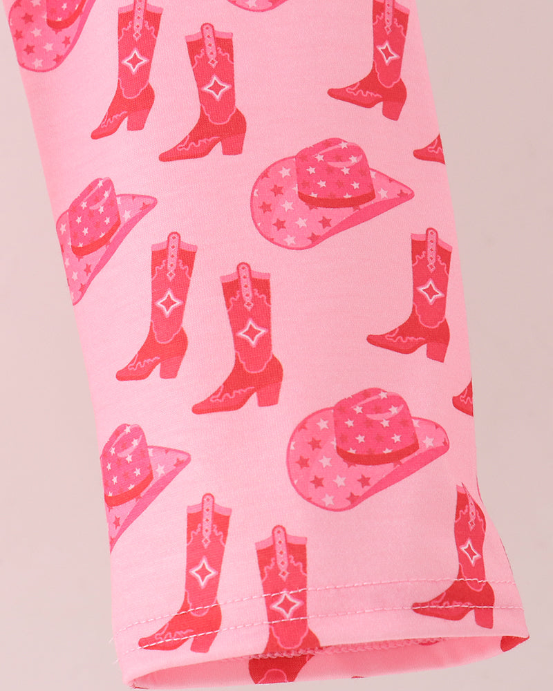 A close-up of a pink leggings, featuring a repeating pattern of red cowboy boots and pink cowboy hats with white stars and monogram-style details.