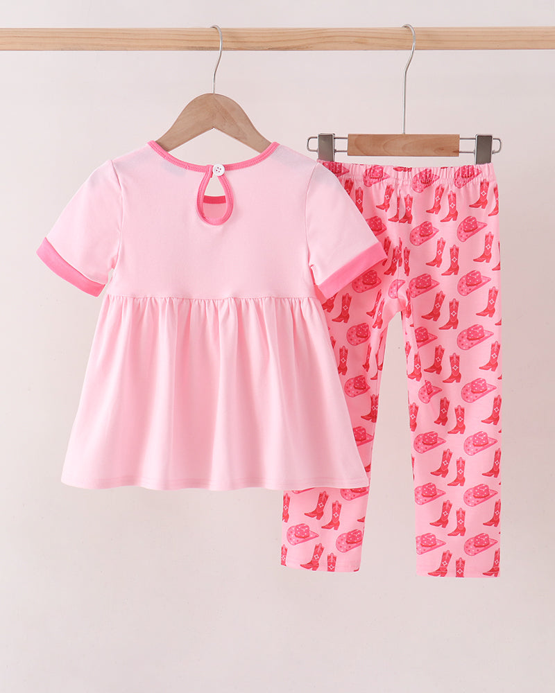 A two-piece baby clothing set hanging on wooden hangers against a plain light background. The set includes a short-sleeve pink dress with a keyhole neckline and matching pink leggings featuring a red cowboy boot print.