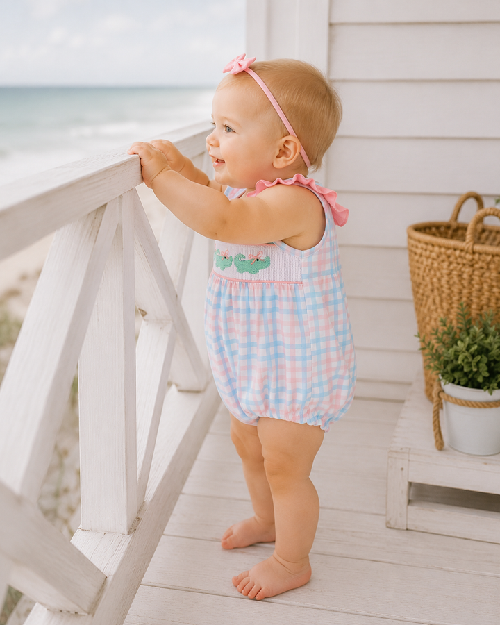 Baby wearing pink-and-blue gingham bubble romper with pink bow and ruffled shoulder neckline