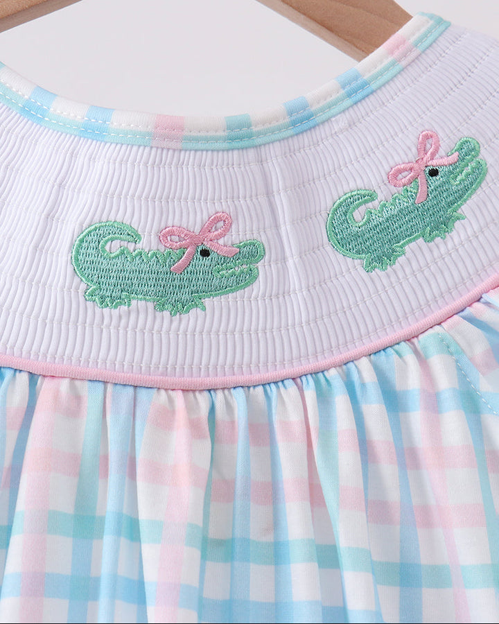Smocked neckline gingham dress with colorful alligator embroidery and pink trim.