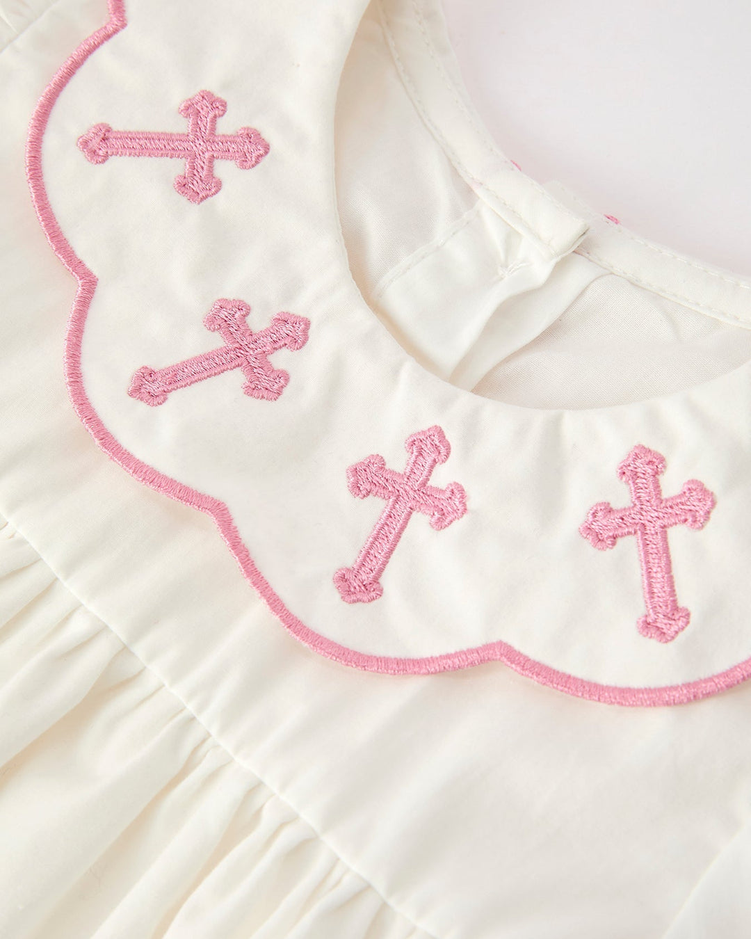 White christening dress bib with pink cross embroidery and scalloped pink edge