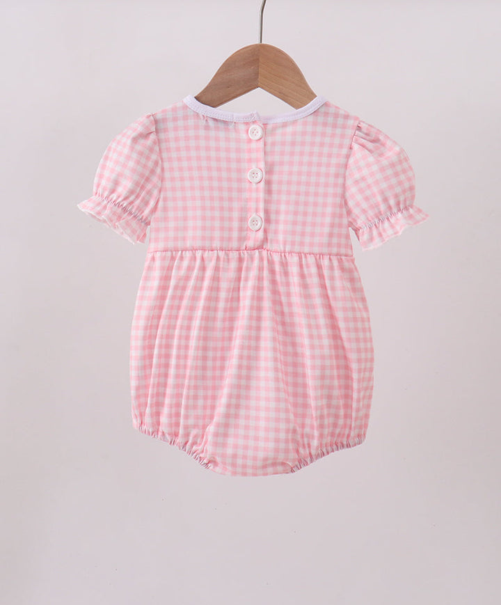 Pink checkered baby romper hanging on a wooden hanger against a light gray background