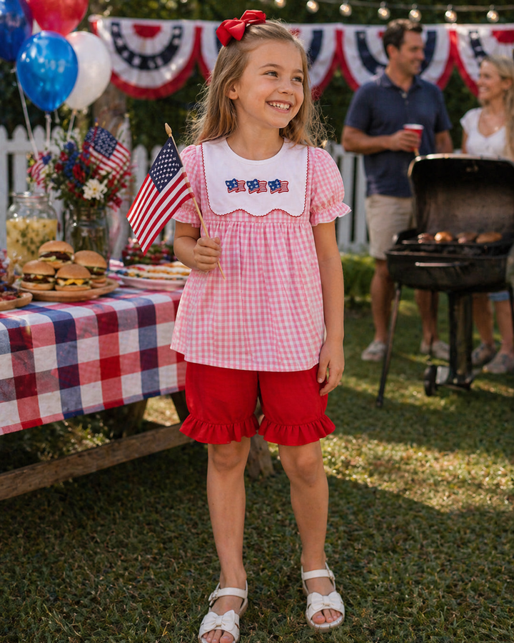 Young girl in a patriotic outfit standing outdoors with a grill and table in the background