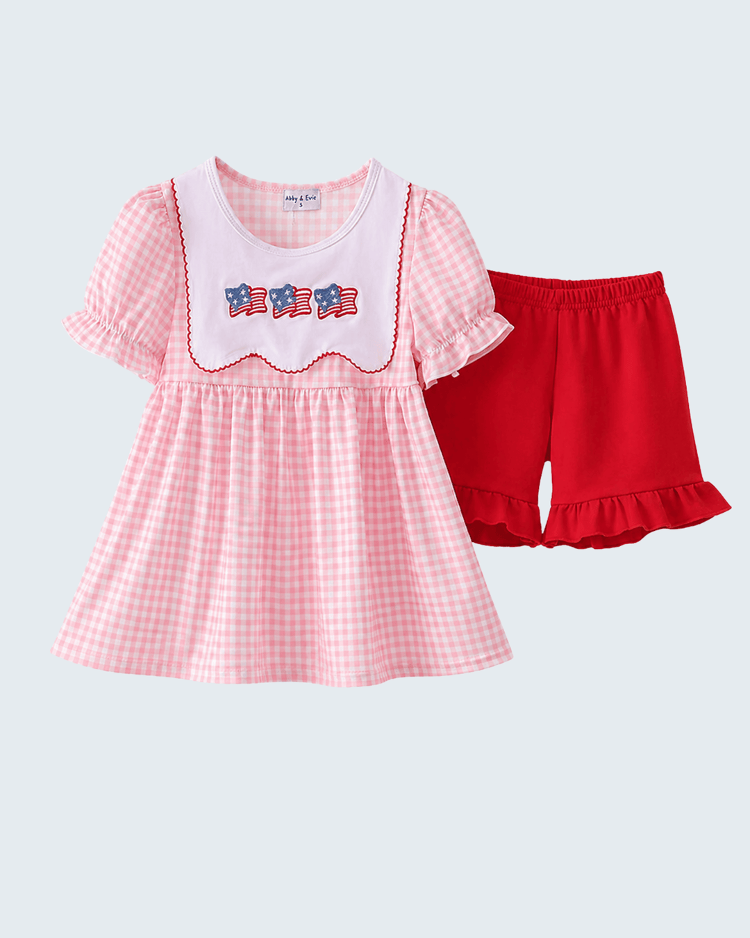 Pink checkered dress with white collar and red shorts on a light gray background