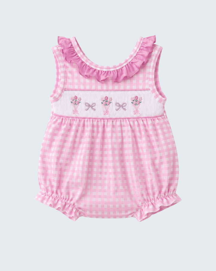 Pink checkered baby romper with floral and bow details on a light gray background