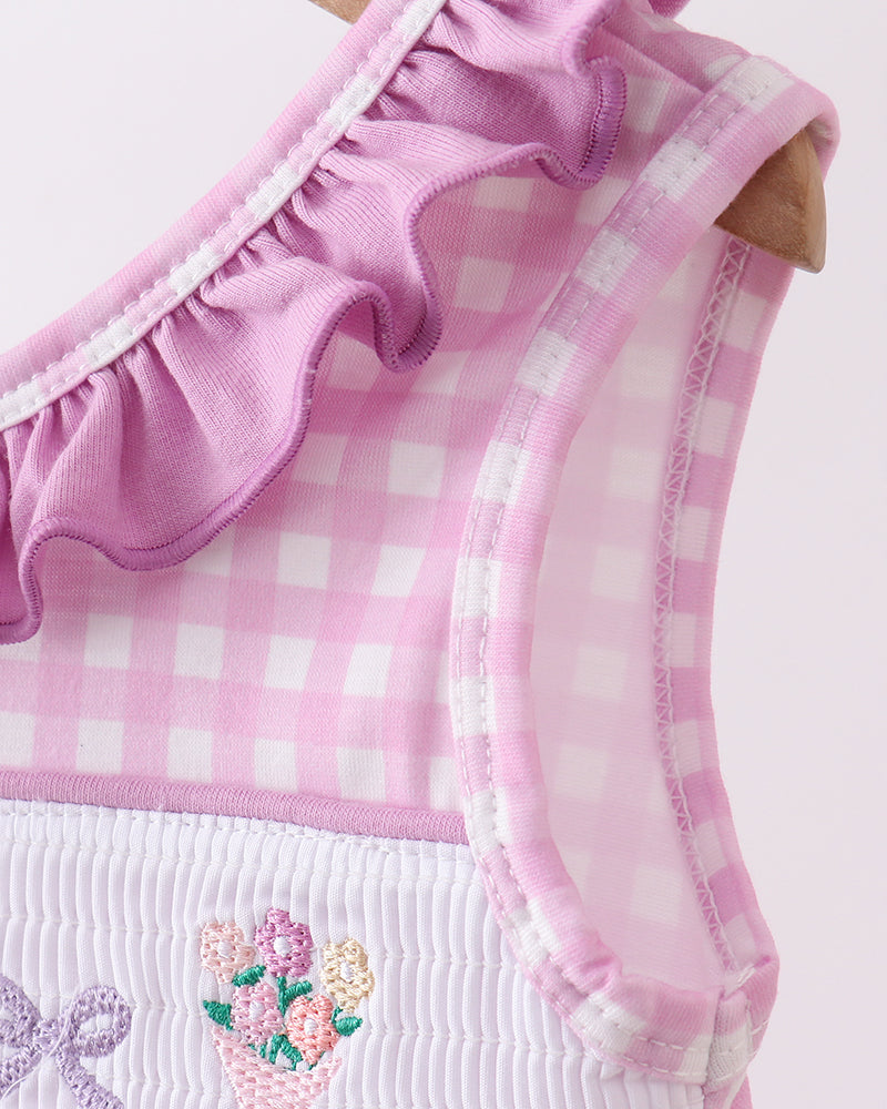 Pink checkered dress with floral embroidery and ruffled details on a light pink background