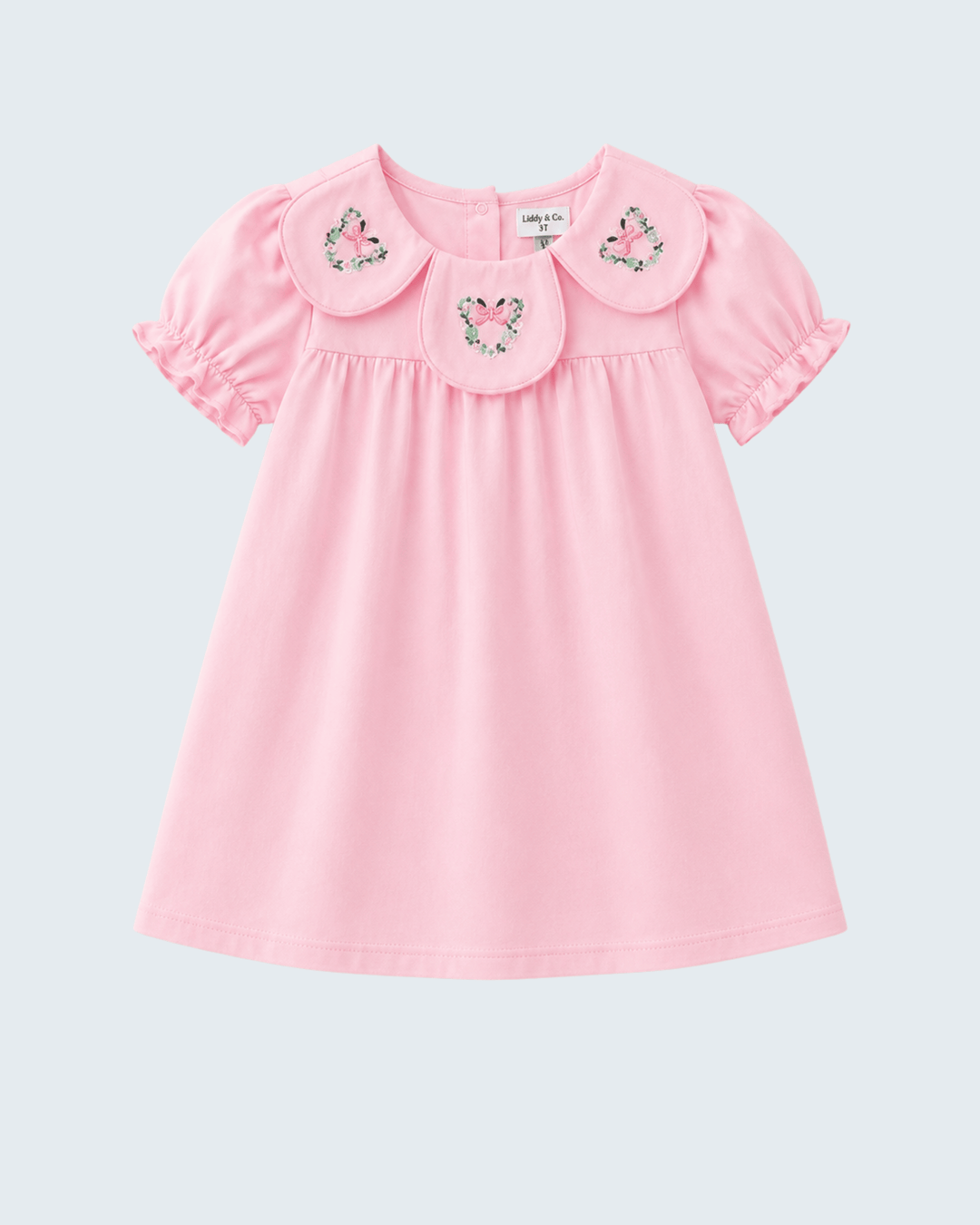 A light pink short-sleeve baby dress with a large Peter Pan collar decorated with three embroidered floral motifs, shown against a light gray background.