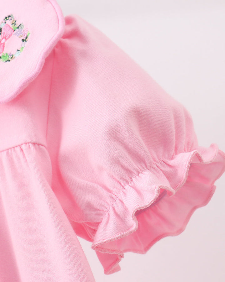 Close-up of a light pink garment featuring a ruffled short puff sleeve and a matching ruffled collar with a small floral embroidered detail.
