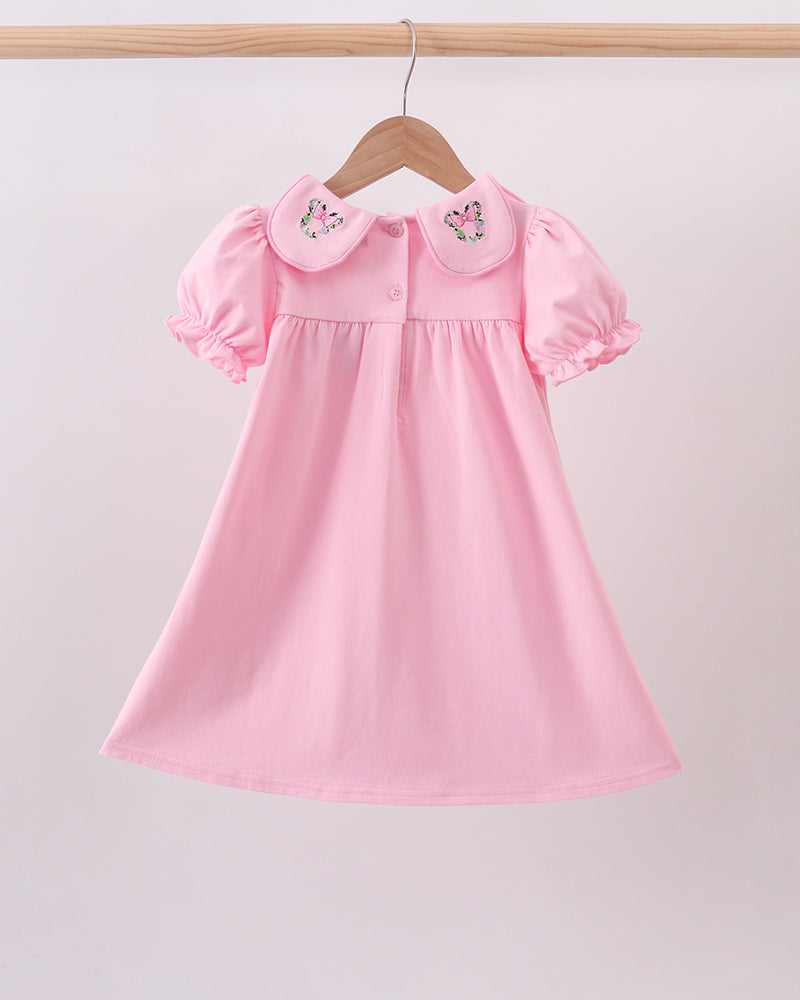 A pink short-sleeve baby dress with a Peter Pan collar and embroidered butterfly details, hanging on a wooden hanger against a light gray background.