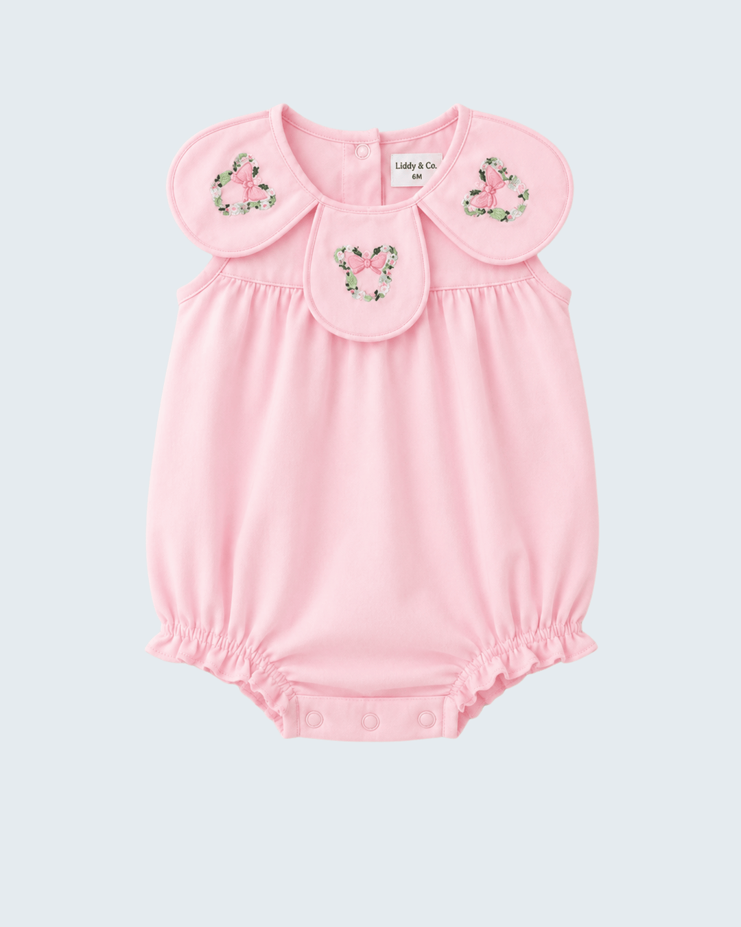 A light pink baby romper with a Peter Pan collar decorated with three pink bow appliques and small green floral details, shown on a light gray background.