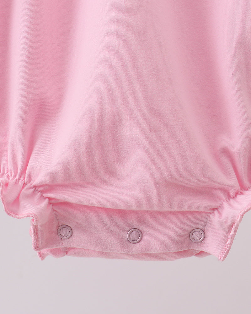 Close-up of a light pink baby bodysuit or romper showing the bottom snap closure with three silver metal snaps on a light gray background.
