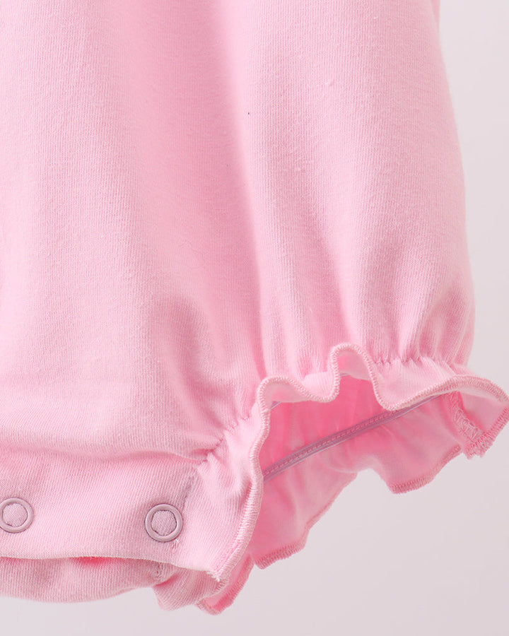 Close-up of a light pink baby romper or bodysuit showing the gathered leg opening with a ruffled hem and snap closures.