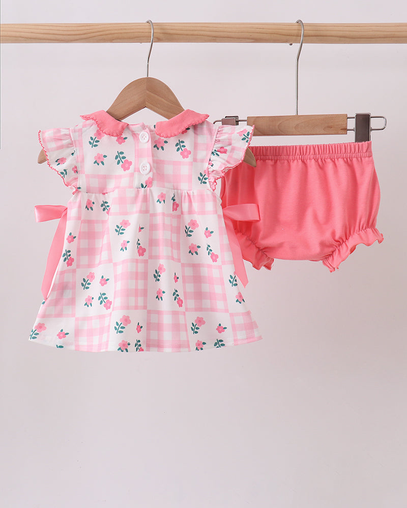 Pink floral dress and bloomers set on a wooden hanger against a light gray background