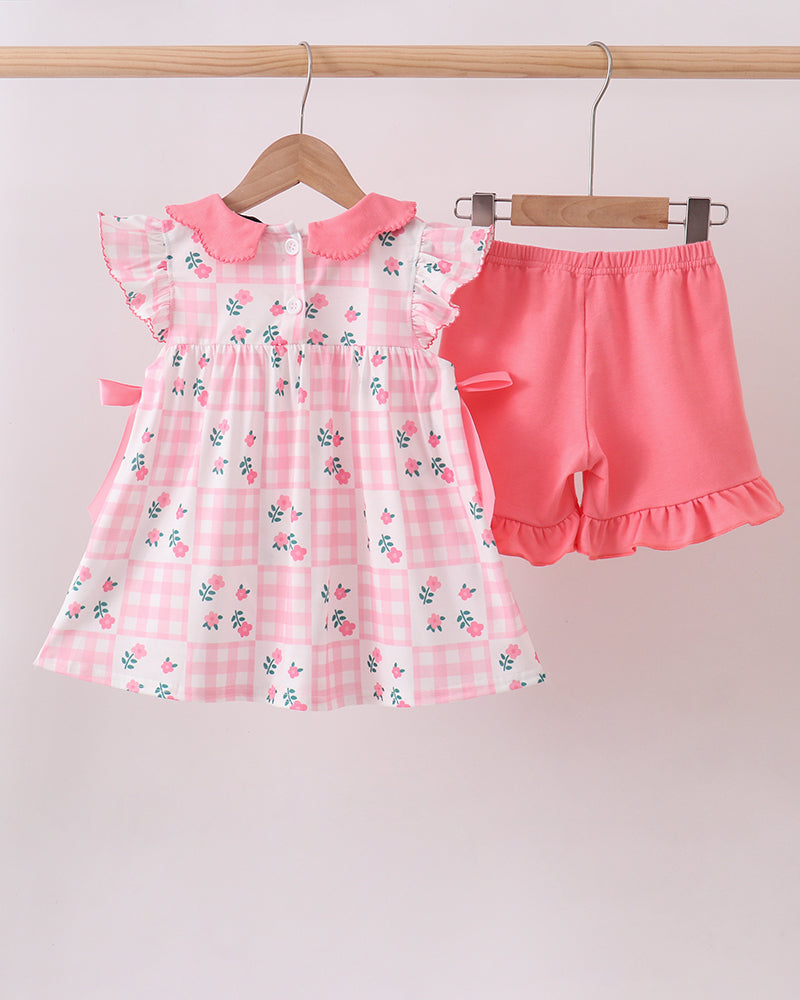Pink checkered dress with floral patterns and matching shorts on hangers against a light gray background