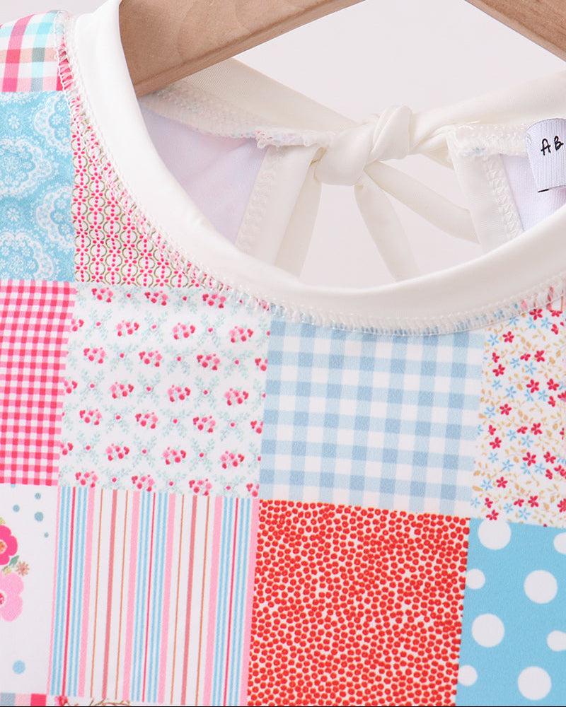 Patchwork rashguard with floral, gingham, and polka dot patterns on a hanger.