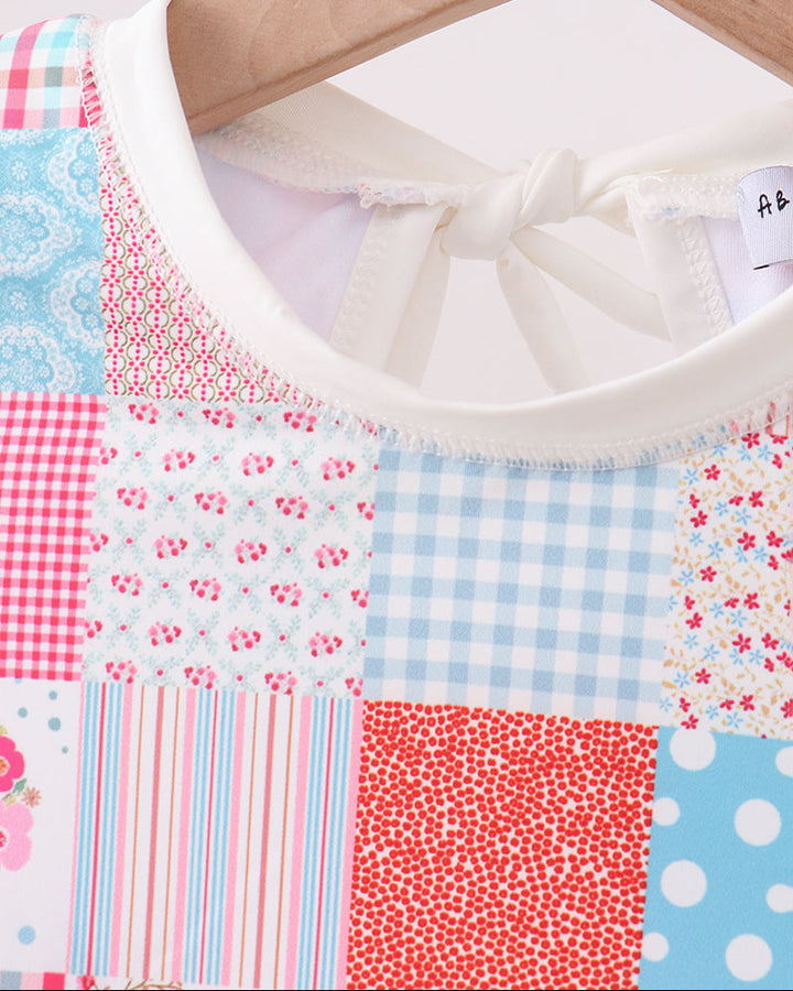 Patchwork rashguard with floral, gingham, and polka dot patterns on a hanger.