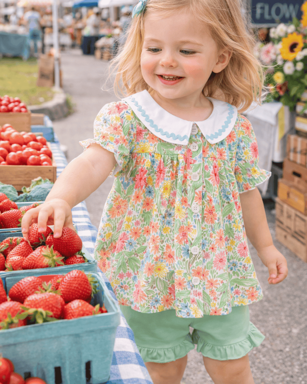 Child in a floral shirt at an outdoor market with strawberries.