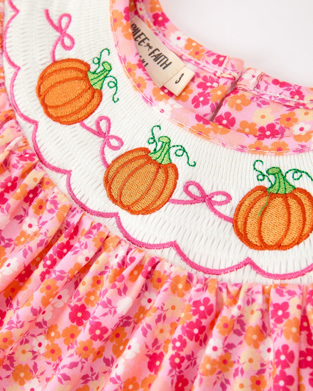 Close-up: embroidered orange pumpkins on white smocked yoke of pink floral dress