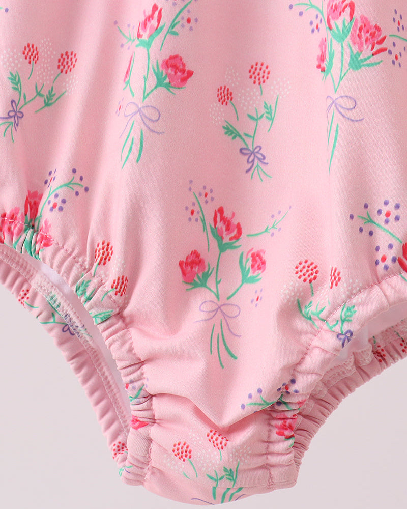 Pink swimsuit with floral and bow pattern on a light pink background