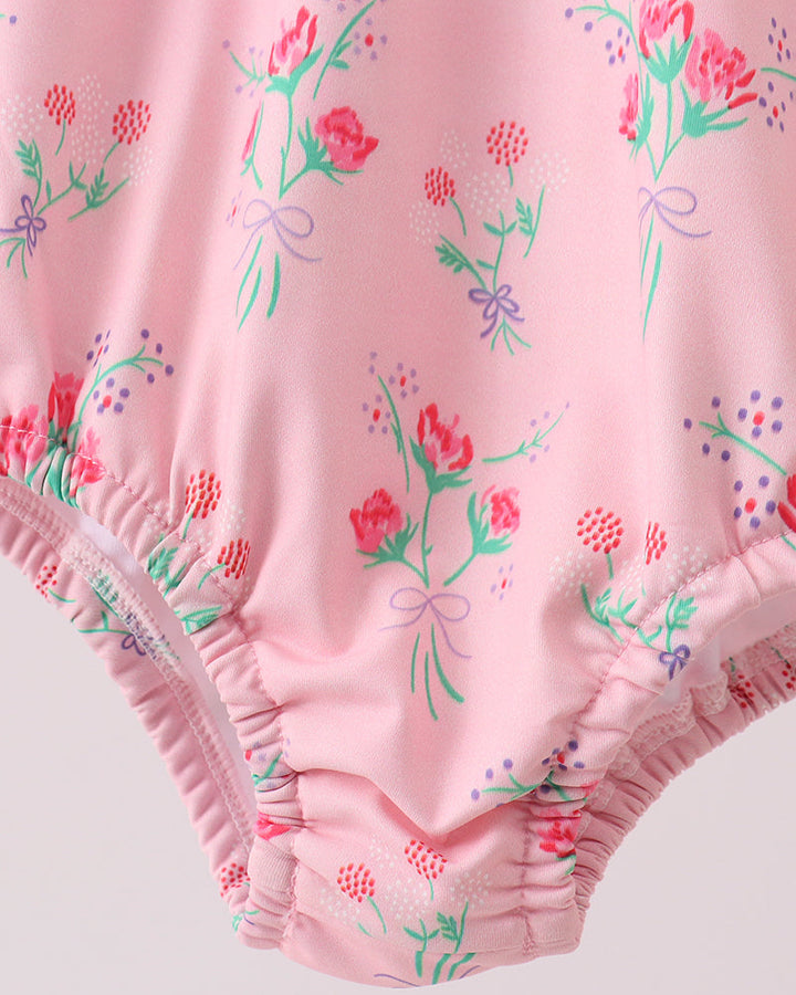 Pink swimsuit with floral and bow pattern on a light pink background
