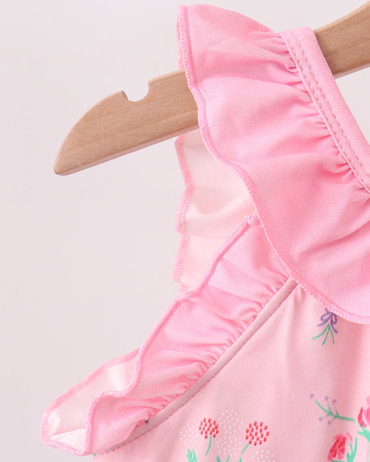 Pink swimsuit with floral embroidery on a wooden hanger against a light pink background