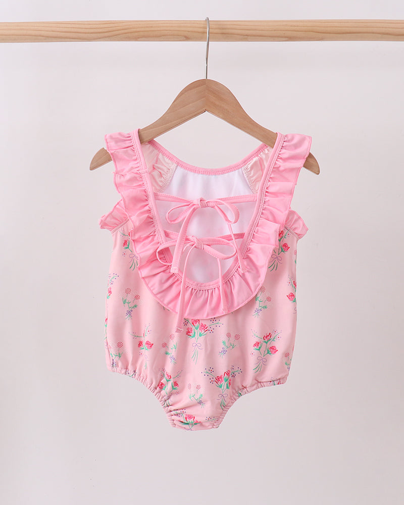 Pink swimsuit with ruffles on a wooden hanger against a white background