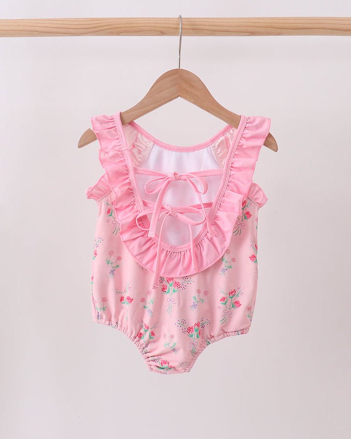 Pink swimsuit with ruffles on a wooden hanger against a white background
