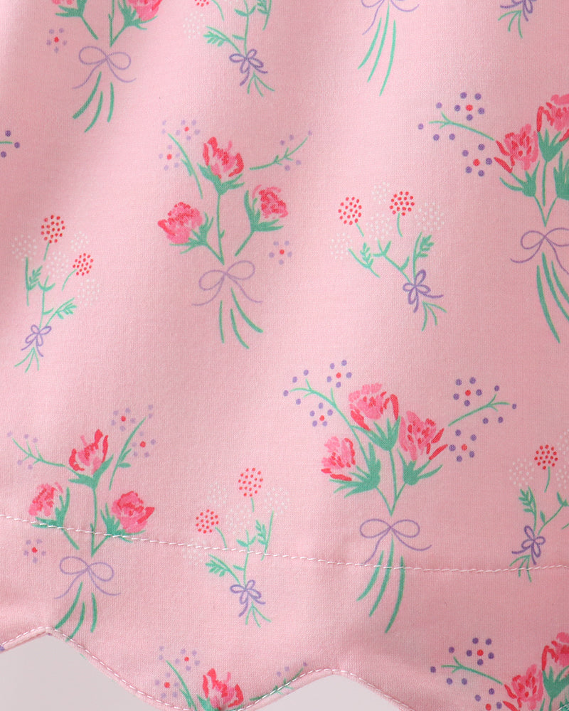 Floral pattern on a pink fabric with green leaves and red flowers.