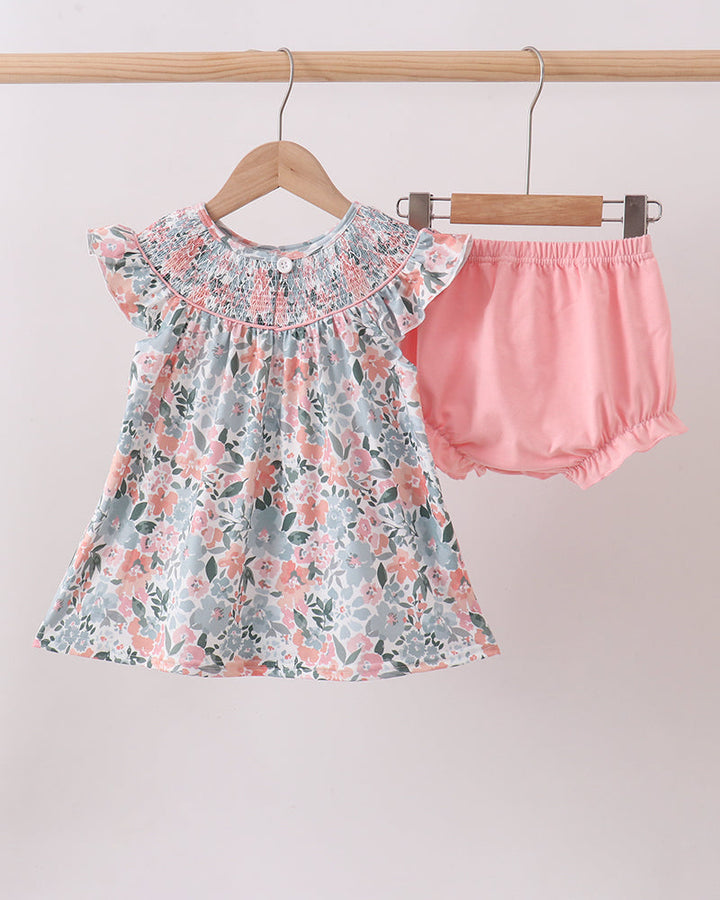 Floral dress and pink bloomers on hangers against a light background
