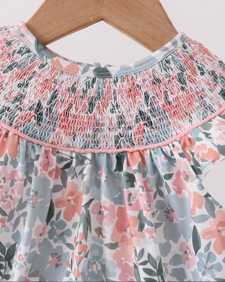 Floral dress with smocked neckline on a wooden hanger against a white background