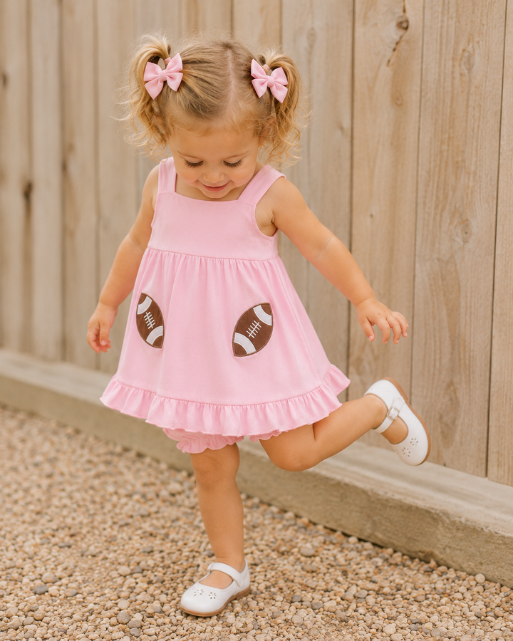 Child wearing pink football applique dress with ruffled skirt and matching shorts