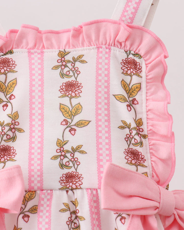 Pink and white baby romper with floral embroidery on a wooden surface