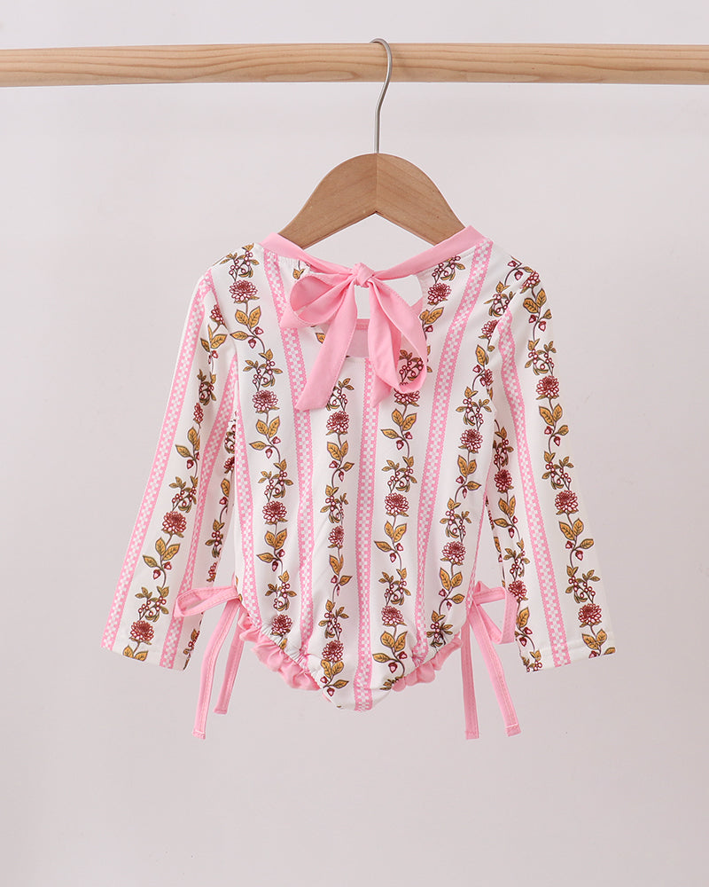 Pink embroidered rashguard with ribbons on a wooden hanger against a light gray background