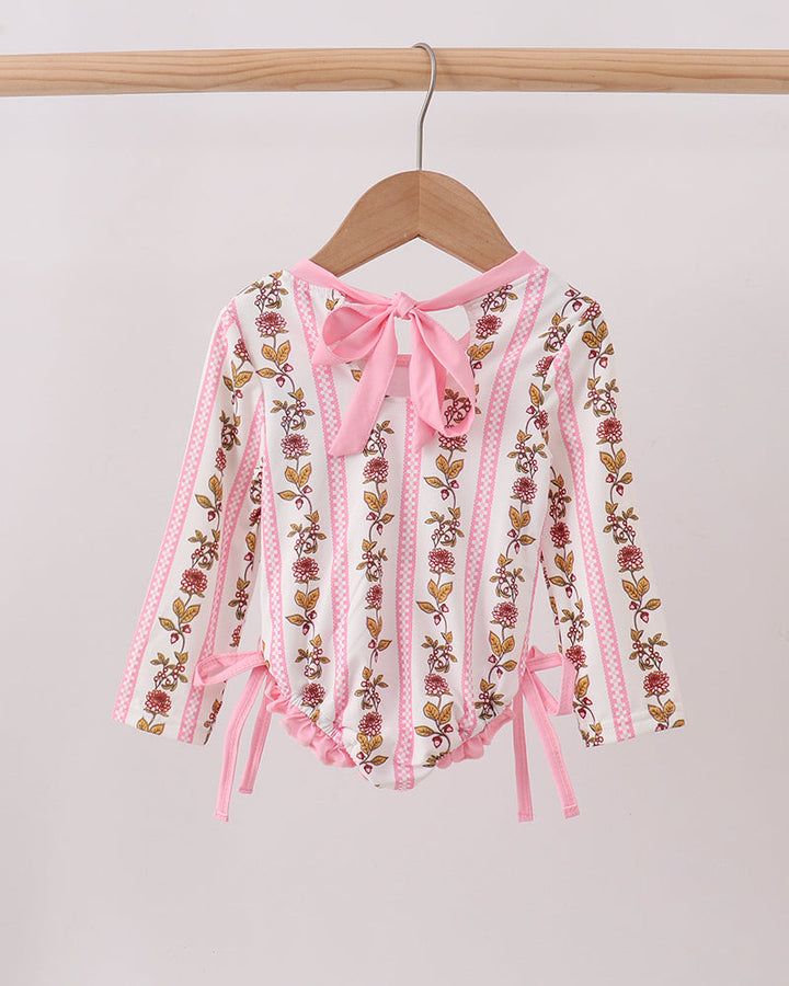 Pink embroidered rashguard with ribbons on a wooden hanger against a light gray background