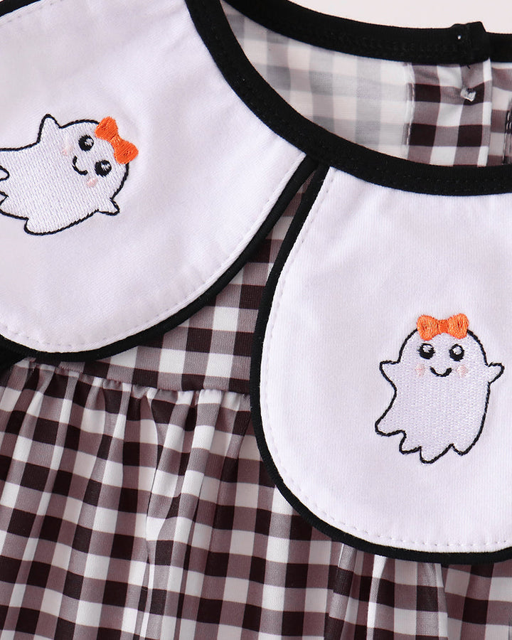 Close-up of a baby dress with a brown and white gingham pattern, featuring two large white Peter Pan collars with black trim and embroidered cute white ghosts wearing orange bows.