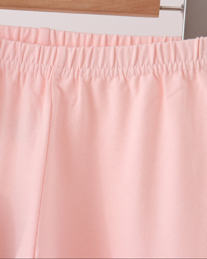 Close-up of a light pink garment, likely shorts or trousers, hanging on a wooden hanger against a plain light background.