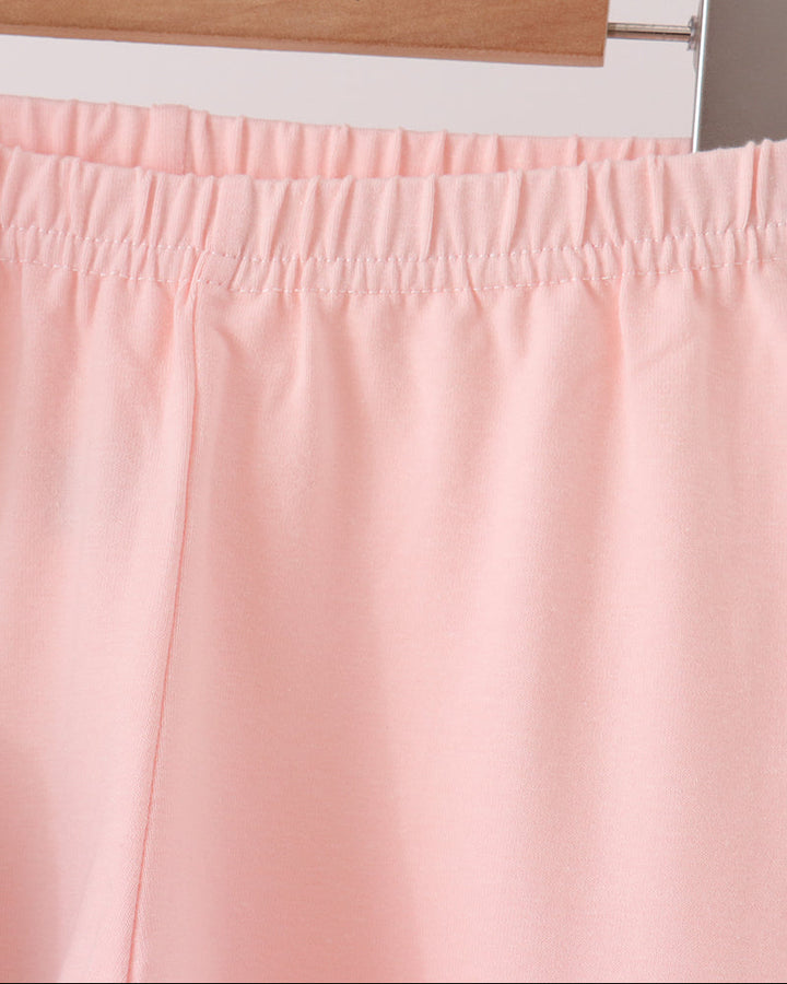 Close-up of a light pink garment, likely shorts or trousers, hanging on a wooden hanger against a plain light background.