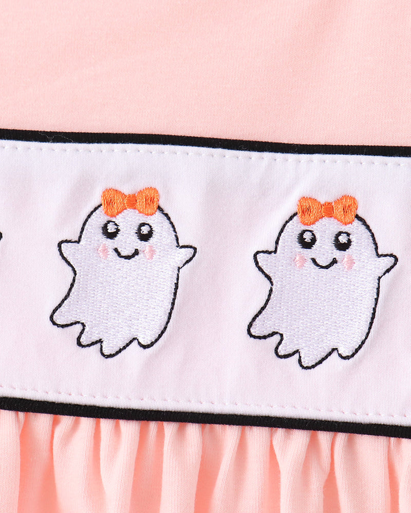 Close-up of a light pink garment featuring a white horizontal band with two embroidered cute white ghosts wearing orange bows, outlined in black.