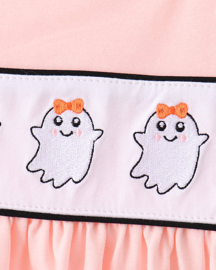 Close-up of a light pink garment featuring a white horizontal band with two embroidered cute white ghosts wearing orange bows, outlined in black.