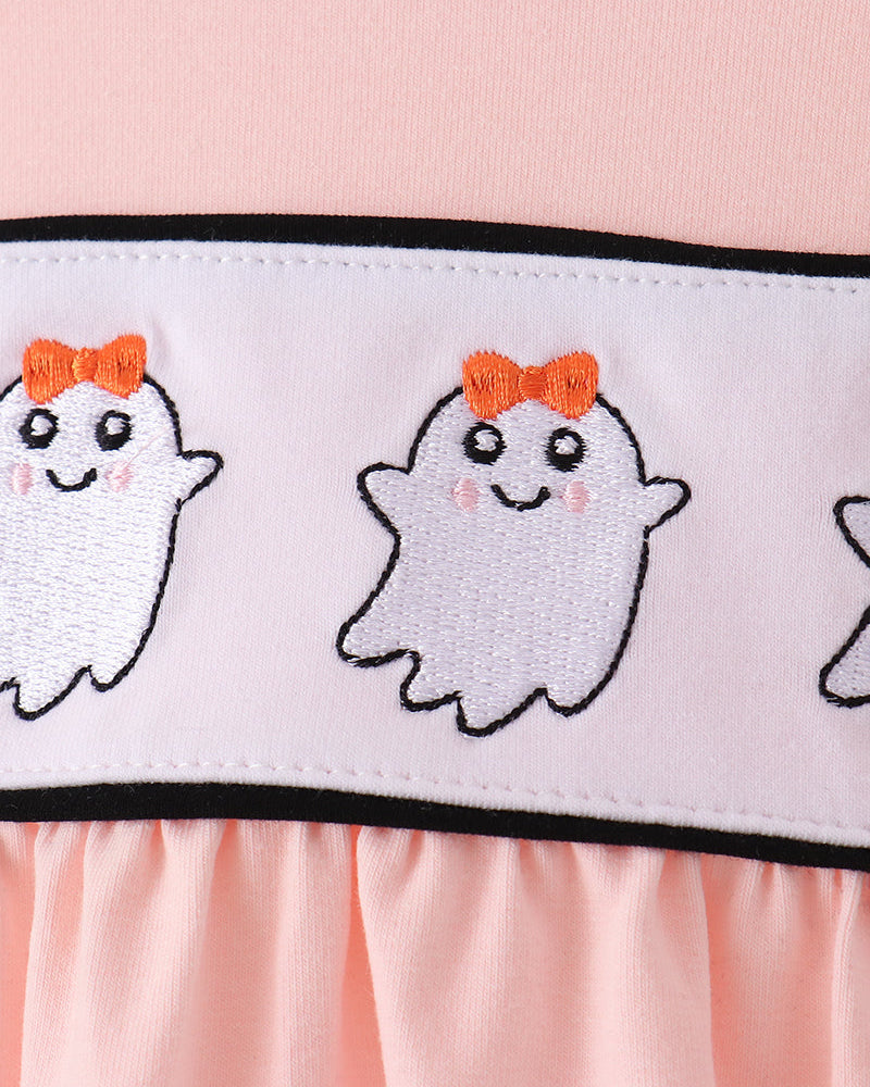 Close-up of a light pink garment with a wide white band featuring embroidered white ghosts with orange bows and black outlines.