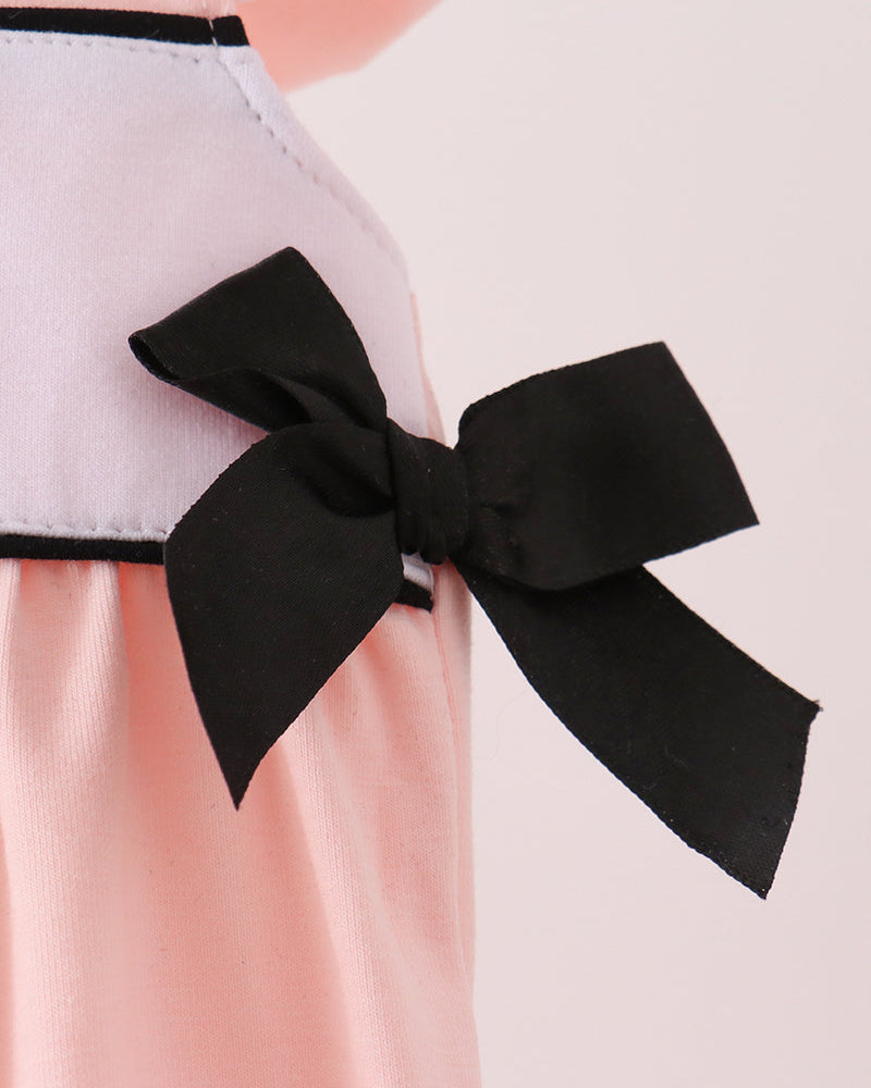 Close-up of a light pink garment with a large black bow at the waist, shown against a pale pink background.