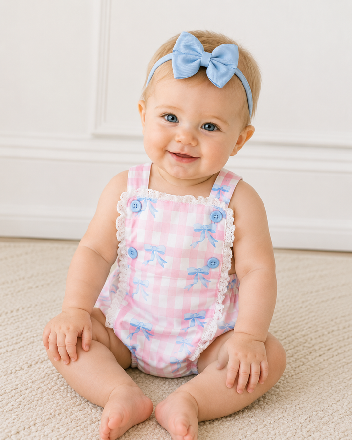 Baby wearing a pink romper with blue floral patterns and a matching headband on a neutral background