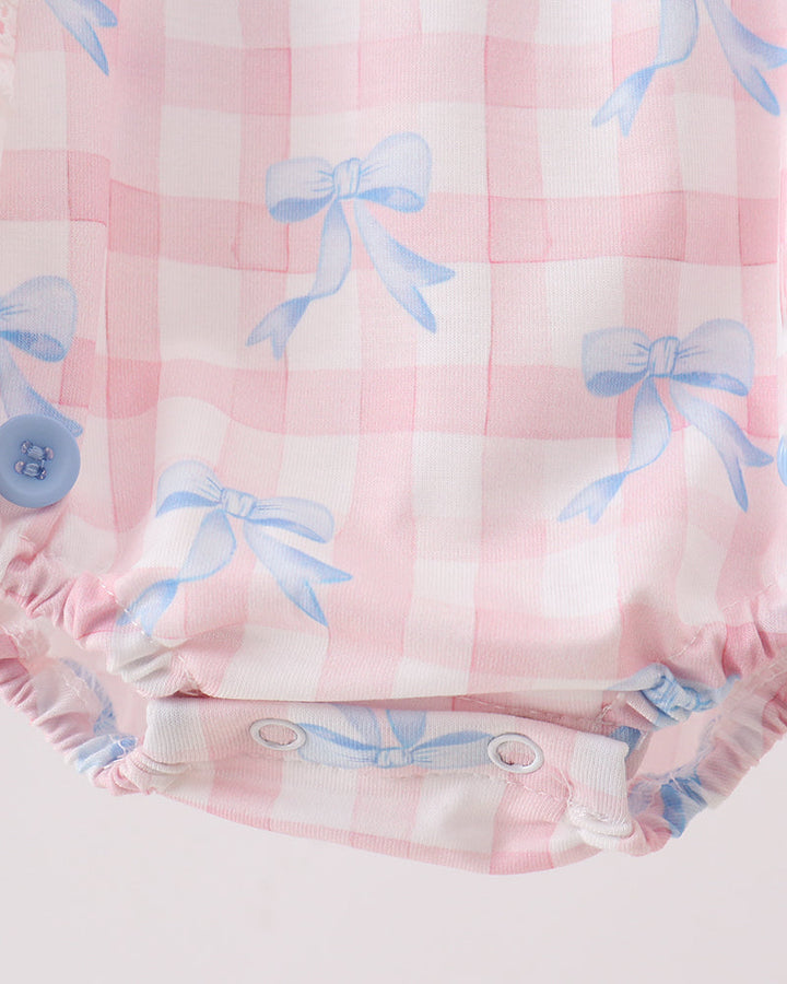 Baby romper with pink checkered pattern and blue bows on a light pink background